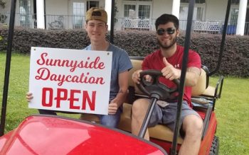 Two Men Holding A Sunnyside Daycare Sign