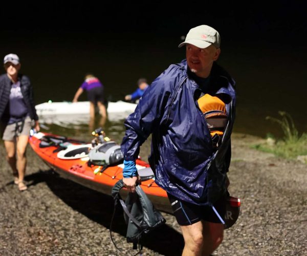 Two Men Carrying Their Tandem Kayak Out Of The Water At Night