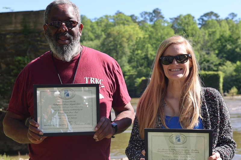 A man and a woman holding awards near a river