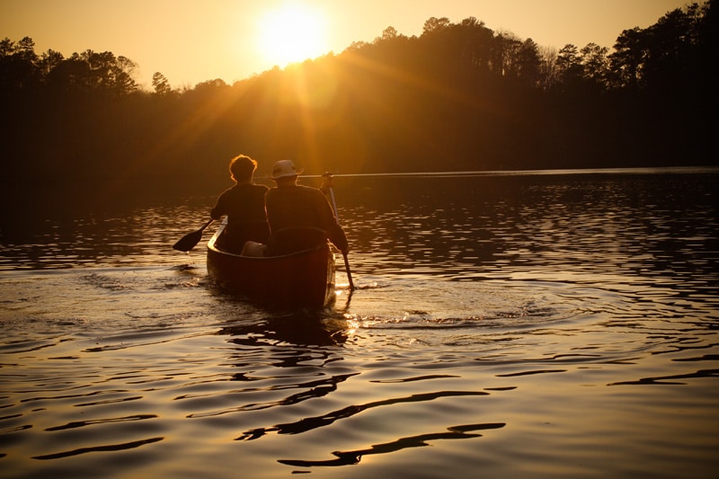 Men riding a canoe towards a sunset