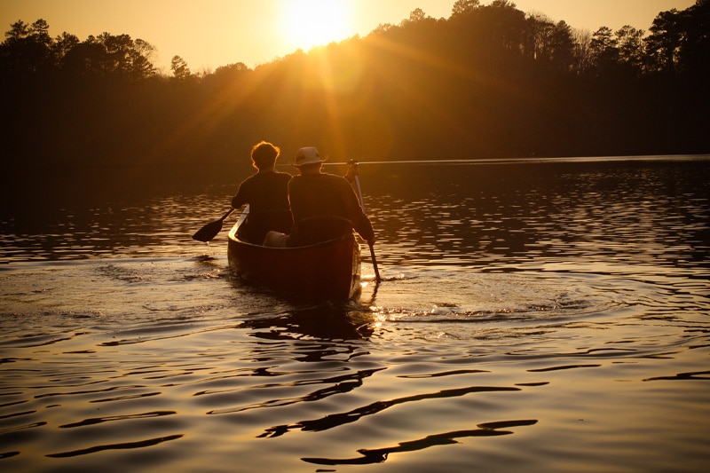 Two men canoeing towards a sunset