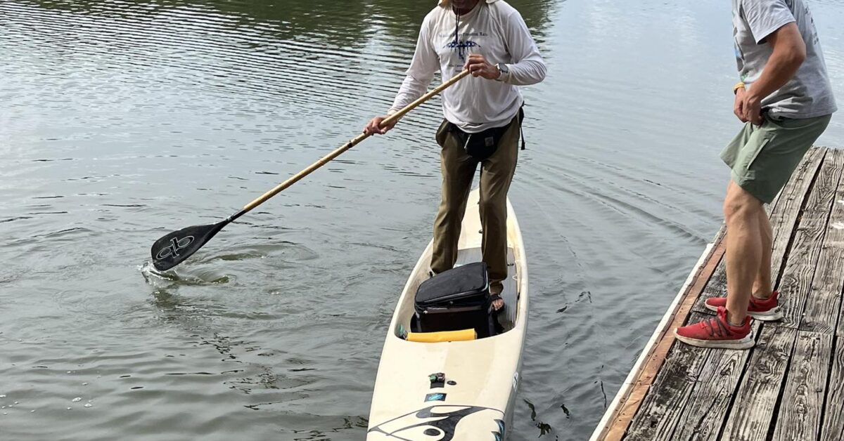 A Man Standing In His Kayak Next To A Pier