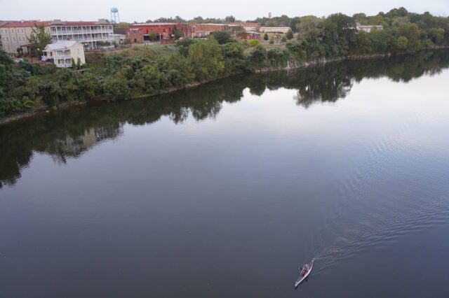 Man Kayaking Down A River Near A Town