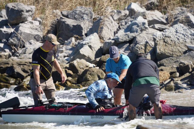 Men Helping A Kayaker Out Of His Boat